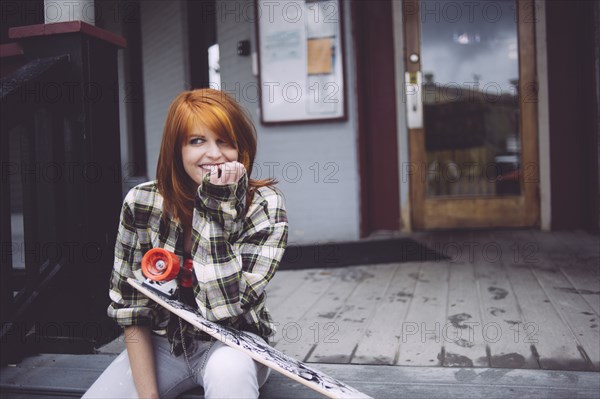 Caucasian woman holding skateboard on patio