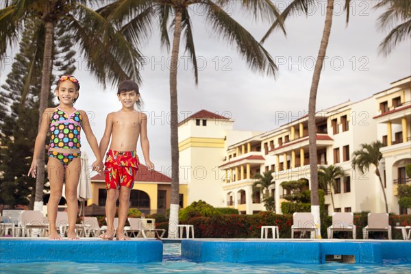 Brother and sister standing at resort poolside holding hands