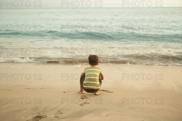 Mixed race boy squatting on beach playing