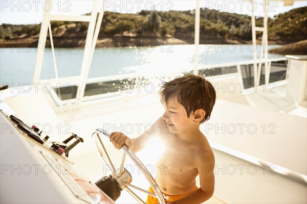 Mixed race boy steering boat on lake