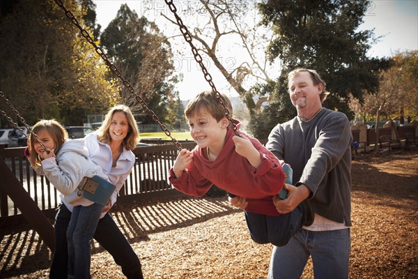 Caucasian parents swinging children on swing set