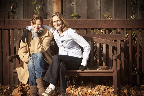 Caucasian friends sitting on bench in autumn