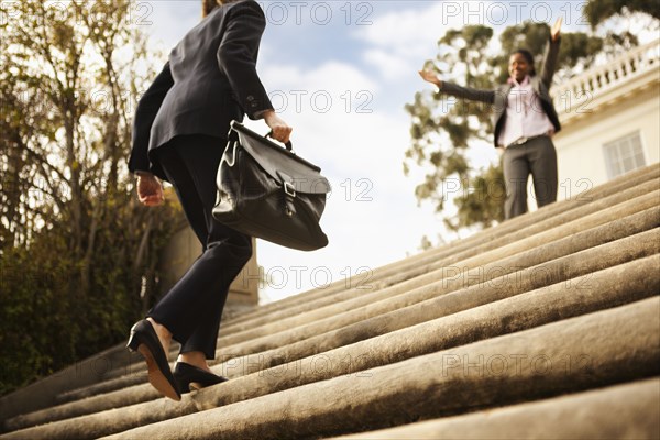 Businesswoman walking up stairs toward co-worker