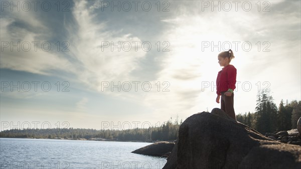 Mixed race girl standing on rock near remote lake