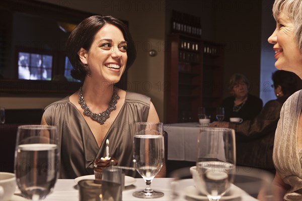 Woman about to blow out birthday cupcake in restaurant