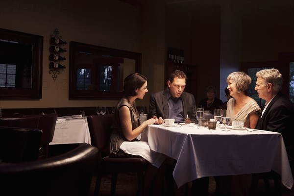 Friends watching man blow out birthday cupcake in restaurant