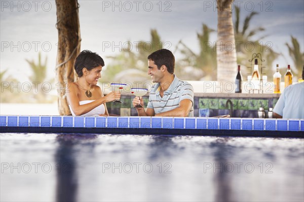 Hispanic couple drinking cocktails at poolside