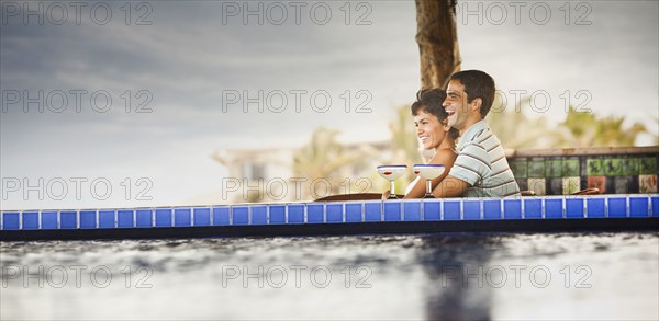 Hispanic couple drinking cocktails at poolside