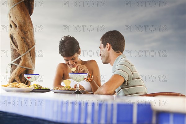 Hispanic couple having dinner at poolside