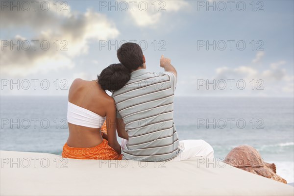 Hispanic couple sitting and looking at ocean
