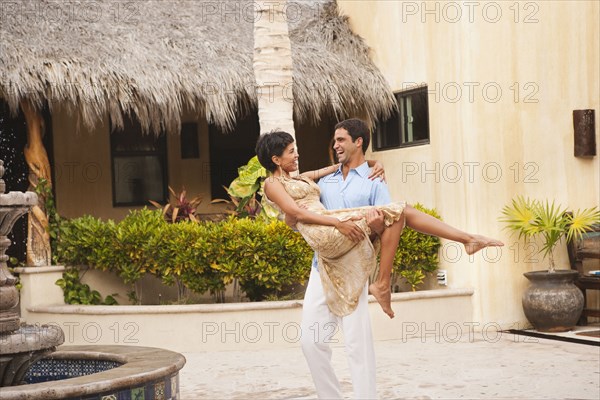 Hispanic man carrying wife in courtyard