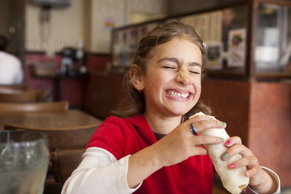 Mixed race girl eating burrito in restaurant