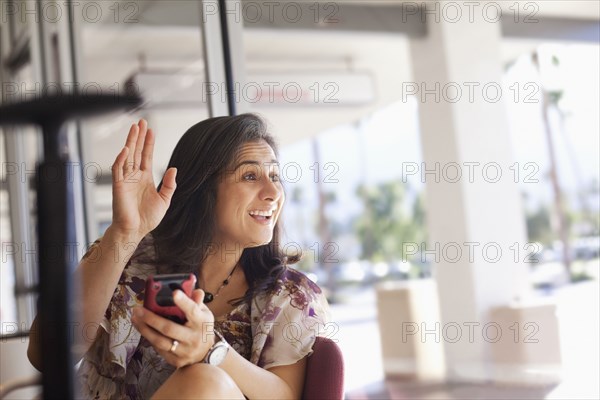 Hispanic woman waving and holding cell phone