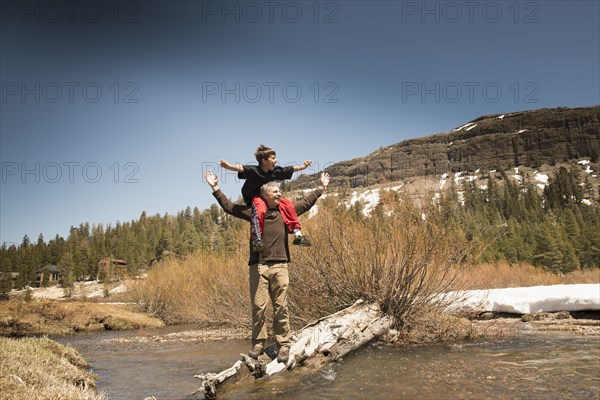 Boy sitting on father's shoulders in creek