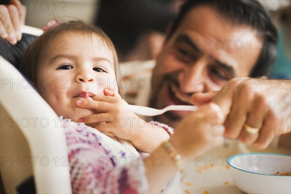 Hispanic father feeding daughter in high chair