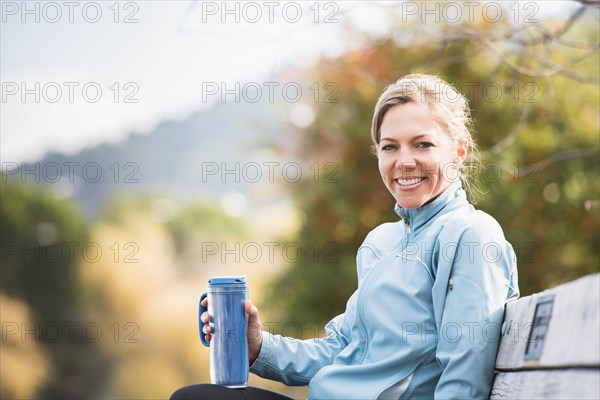 Caucasian woman having coffee on park bench