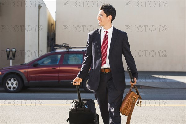 Hispanic businessman rolling luggage