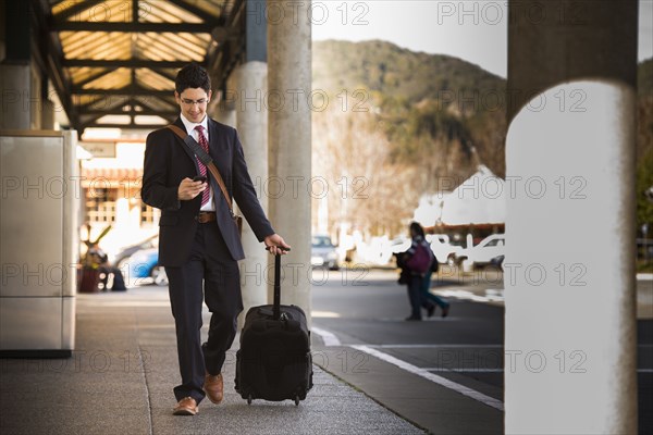 Hispanic businessman rolling luggage