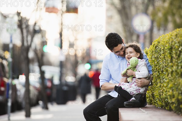 Hispanic father and daughter laughing on city street