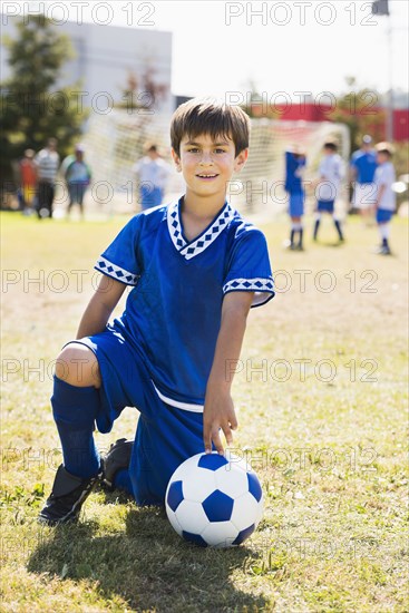 Mixed race boy with soccer ball kneeling on field