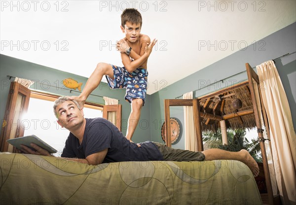 Boy standing on father on bed