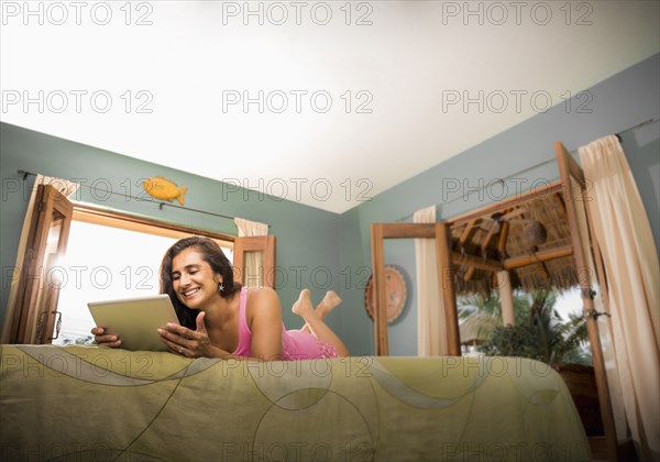 Hispanic woman using digital tablet on bed