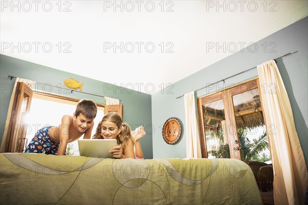 Mixed race children using digital tablet on bed