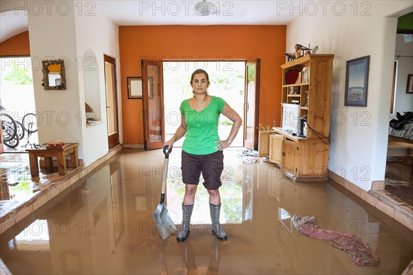 Hispanic woman shoveling water out of flooded house