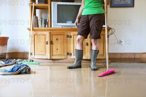 Hispanic woman sweeping water out of flooded house