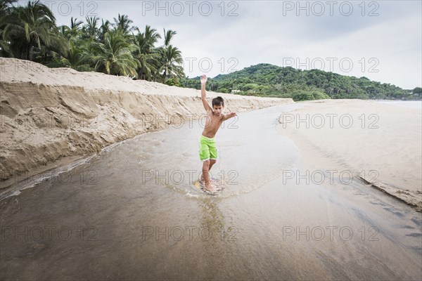 Mixed race boy playing in river on beach