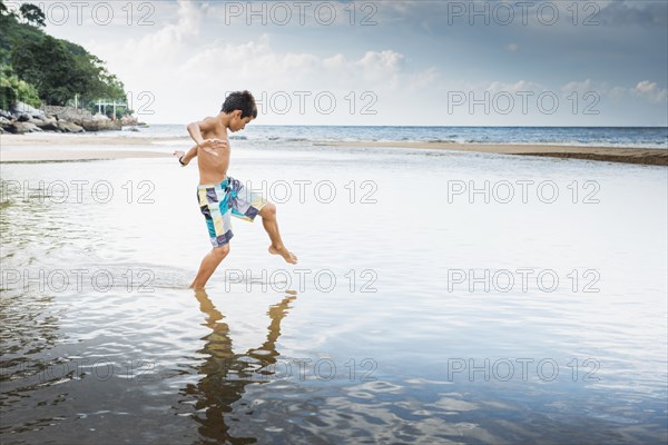 Mixed race boy playing in water on beach