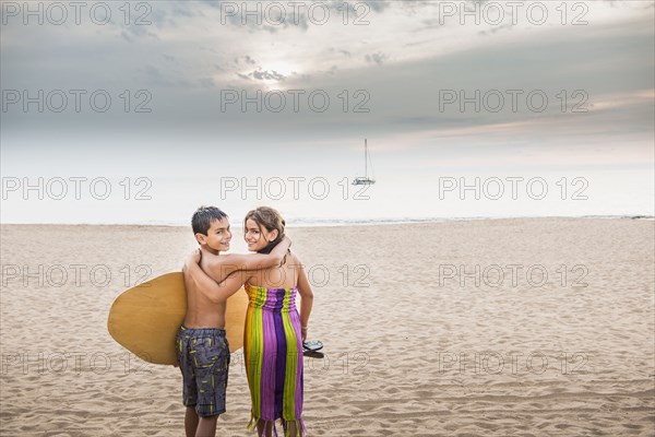 Mixed race children carrying surfboard to ocean