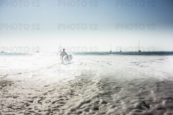 Caucasian man carrying surfboard into ocean