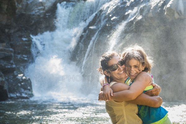 Mother and daughter hugging by waterfall