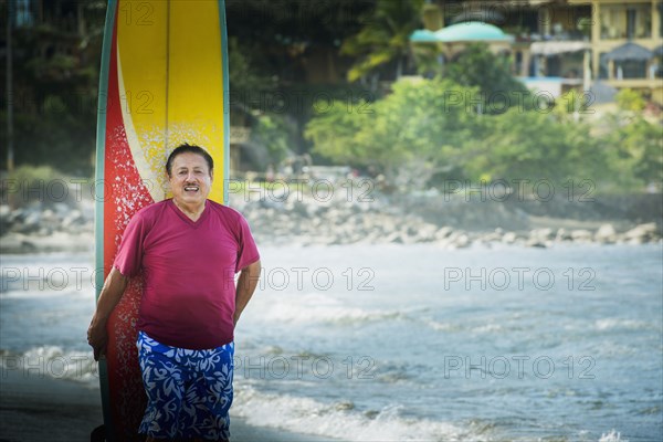 Older Hispanic man with surfboard on beach