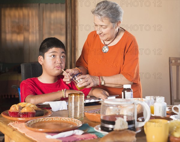 Hispanic woman helping grandson drink through straw