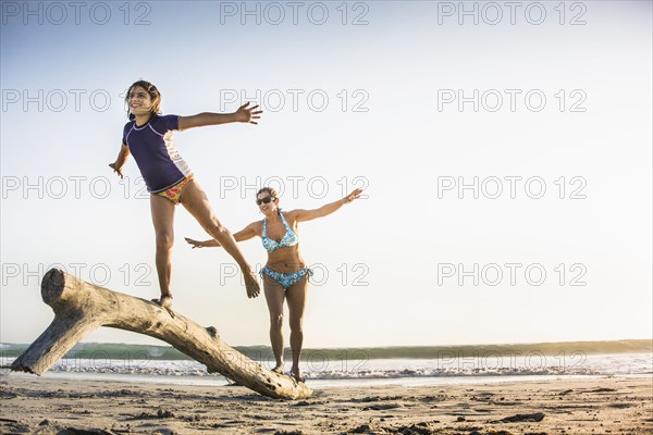 Mother and daughter playing on log on beach