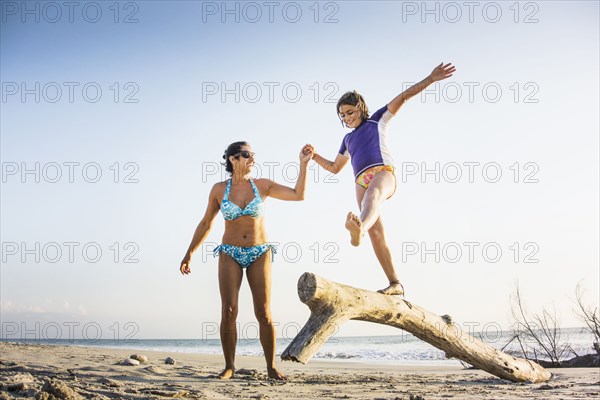 Mother and daughter playing on log on beach