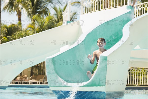 Mixed race boy laughing on water slide