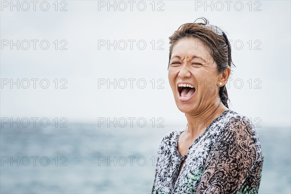 Asian woman laughing near ocean