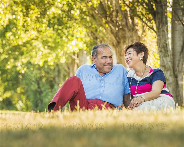 Older Hispanic couple sitting in grassy field