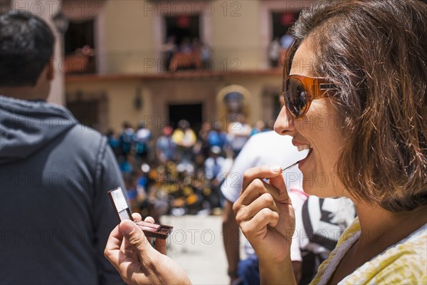 Close up of Hispanic woman applying makeup in mirror outdoors