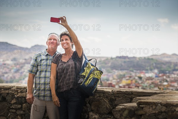 Caucasian couple taking cell phone photograph together on rooftop