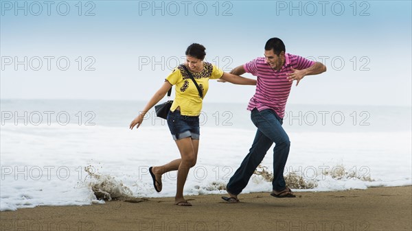 Hispanic couple playing near waves on beach