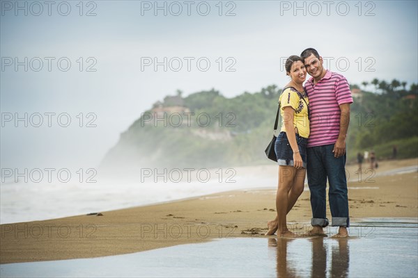 Hispanic couple hugging in waves on beach