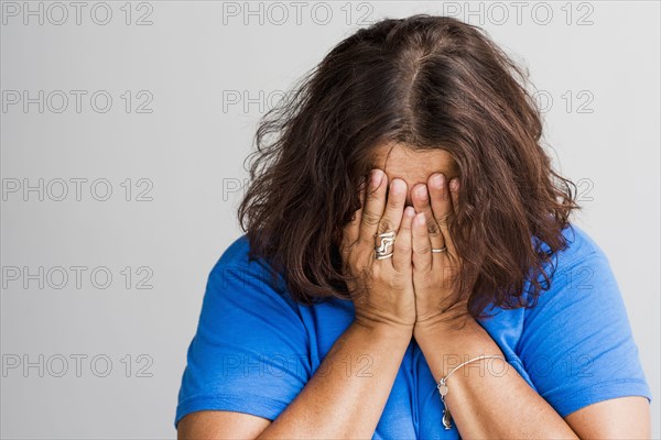 Close up of Hispanic woman covering face with hands