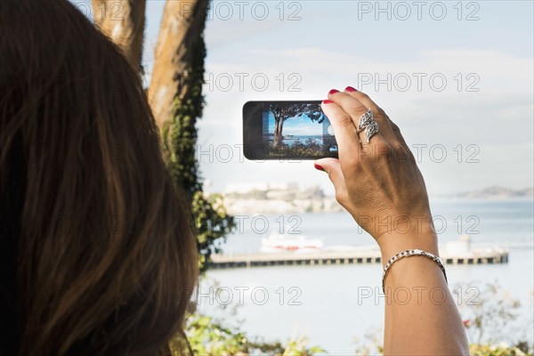 Hispanic woman taking cell phone photograph of beach