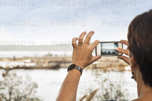 Woman taking cell phone photograph of beach