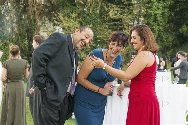 Hispanic friends using cell phone at wedding