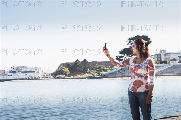 Hispanic woman taking cell phone selfie at waterfront